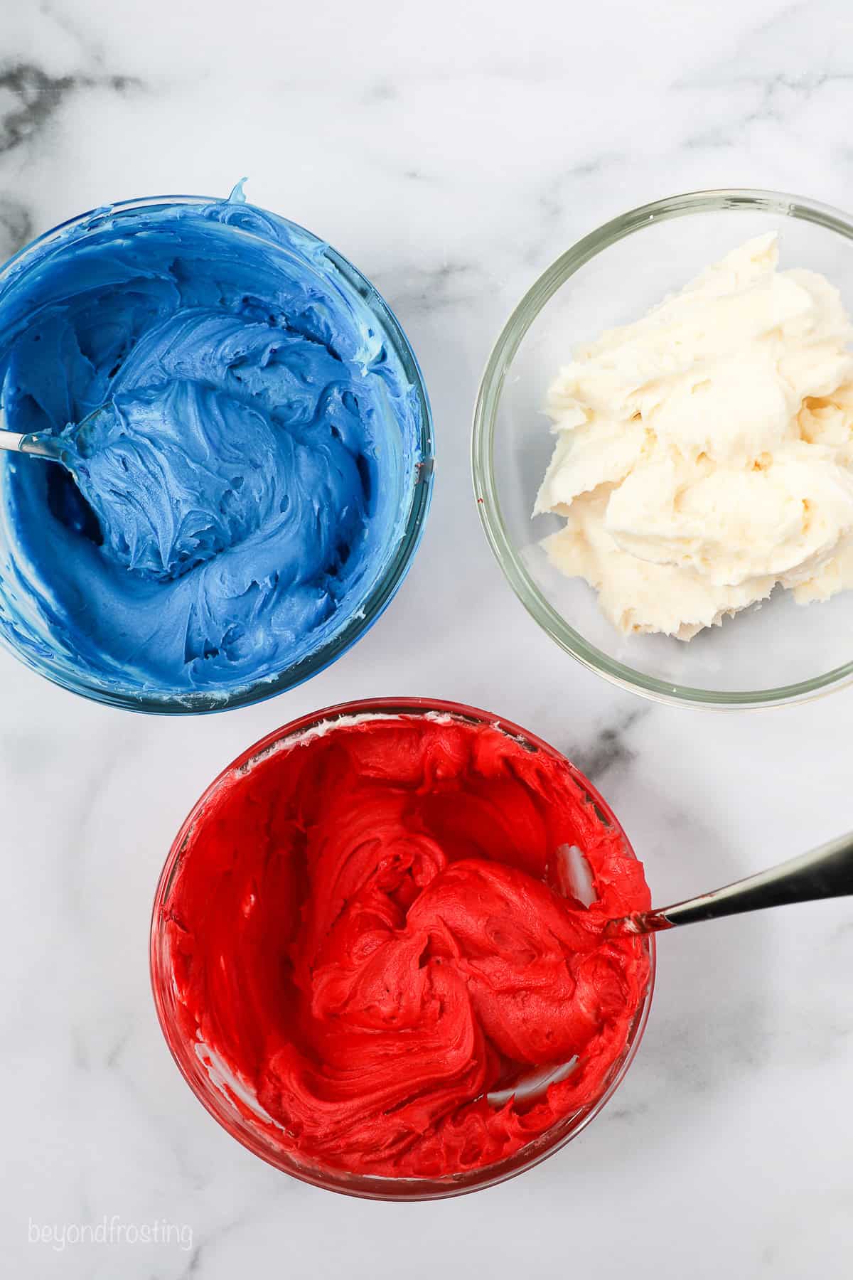 Overhead view of three bowls of red, white, and blue colored frosting.