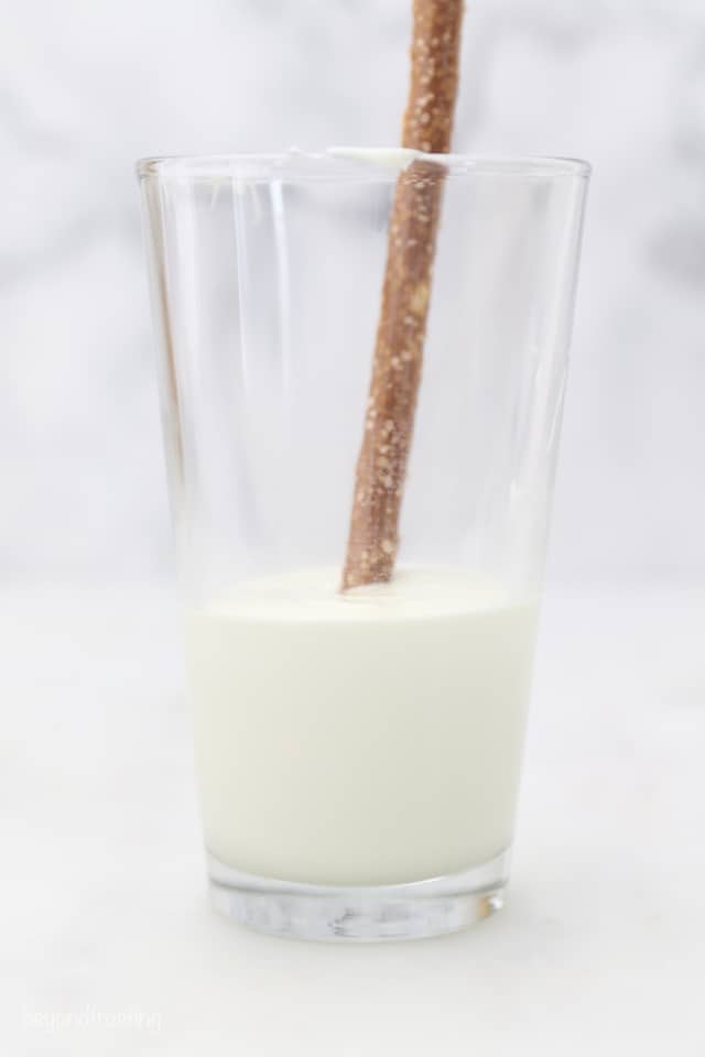 A glass half full of white chocolate with a pretzel stick