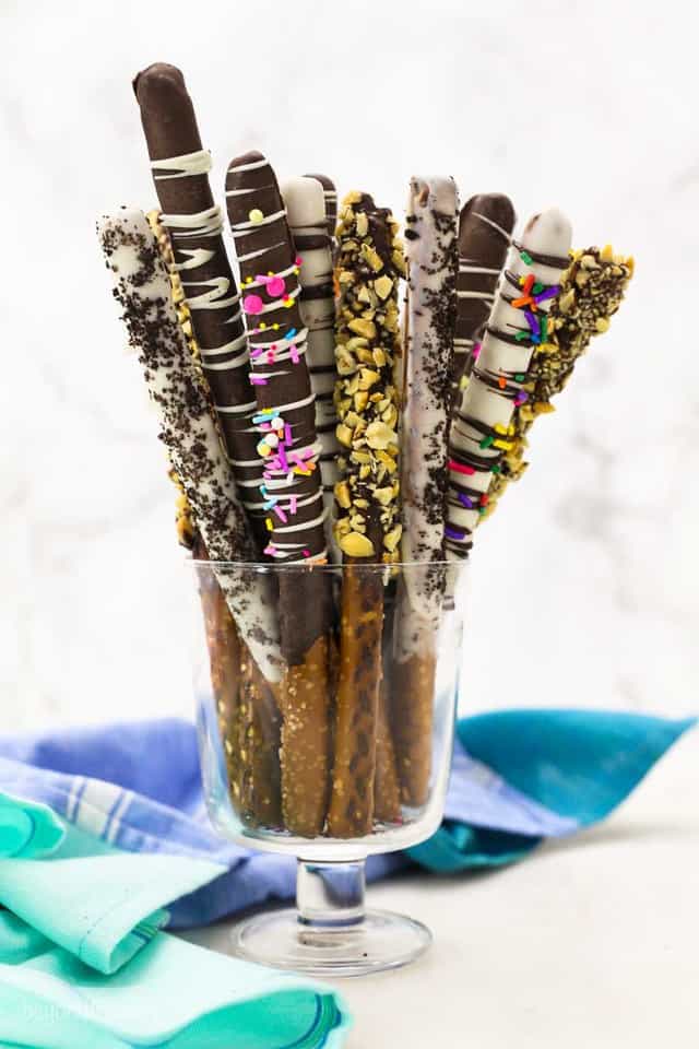 A glass full of chocolate covered pretzel rods in a variety of colors
