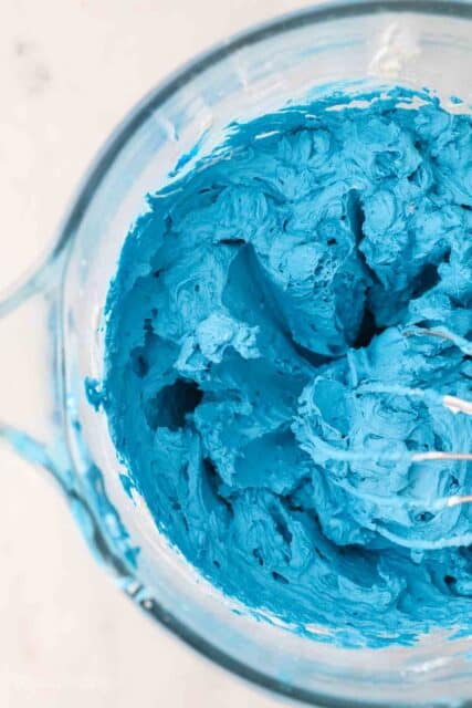 an overhead shot of a glass mixing bowl filled with blue frosting