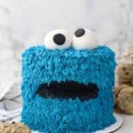 a cookie monster cake sitting on a marble surface with a jar of cookies in the background