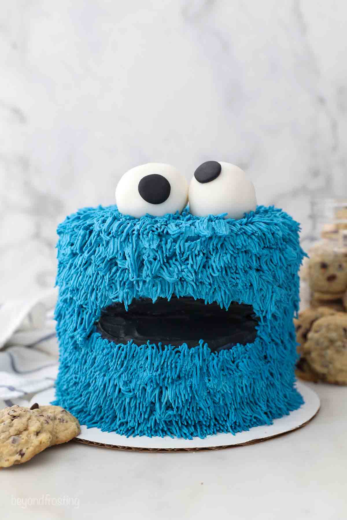 a cookie monster cake sitting on a marble surface with a jar of cookies in the background