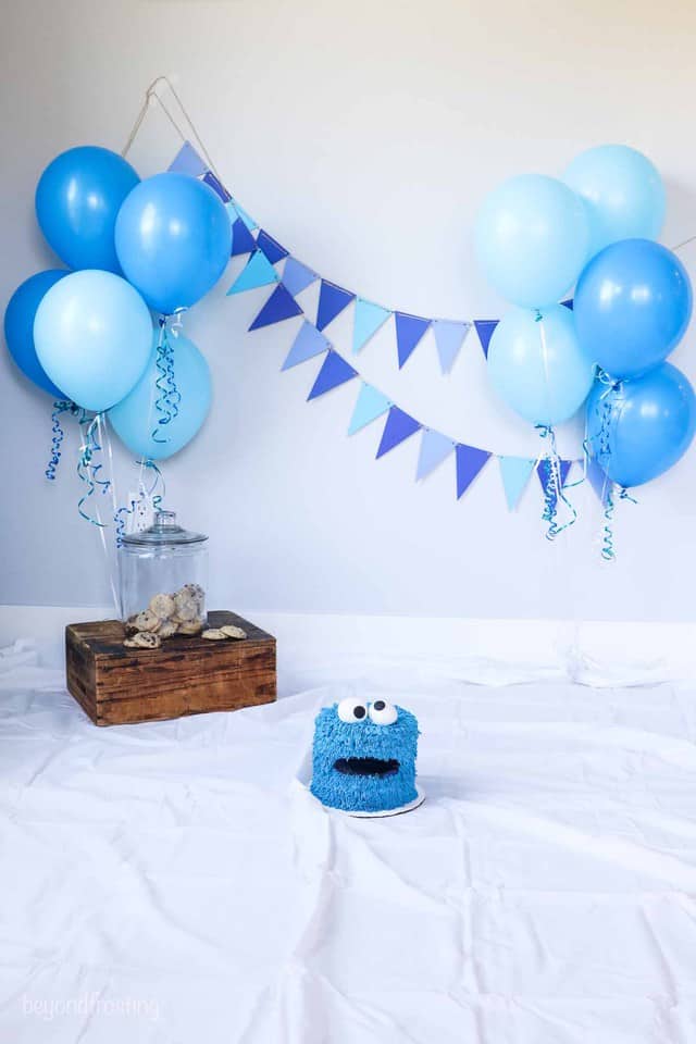 a setup for a cookie monster themed smash cake with balloons and blue bunting on the wall
