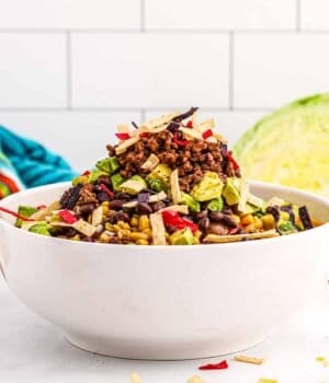 A big bowl of taco salad piled with veggies, tortillas, avocado and ground beef