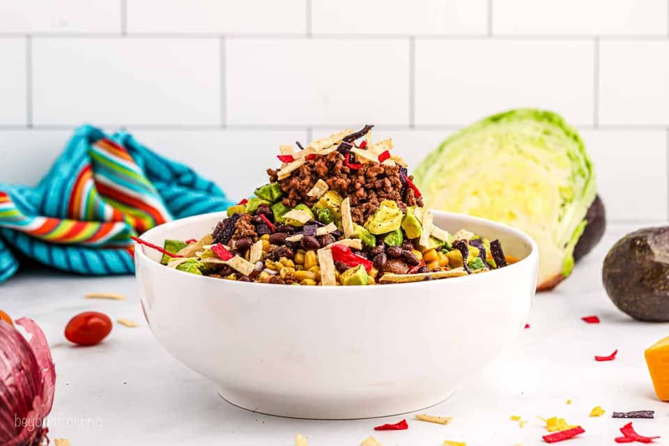 A big bowl of taco salad piled with veggies, tortillas, avocado and ground beef