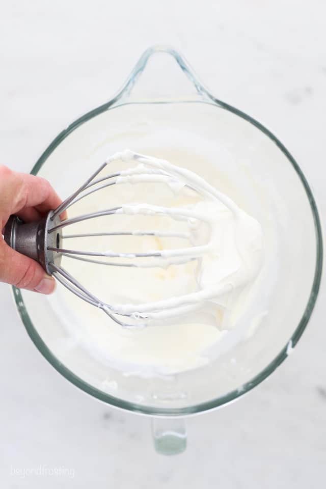a whisk attachment handing over a glass mixing bowl of whipped mascarpone cheese