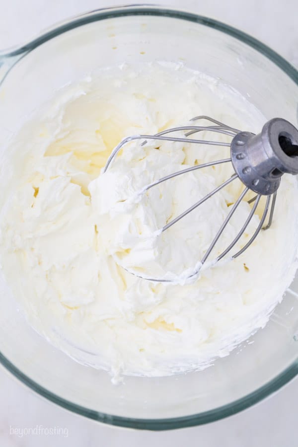 a glass mixing bowl with a whisk attachment and whipped cream