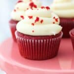 a pink cake stand with red velvet cupcakes on top