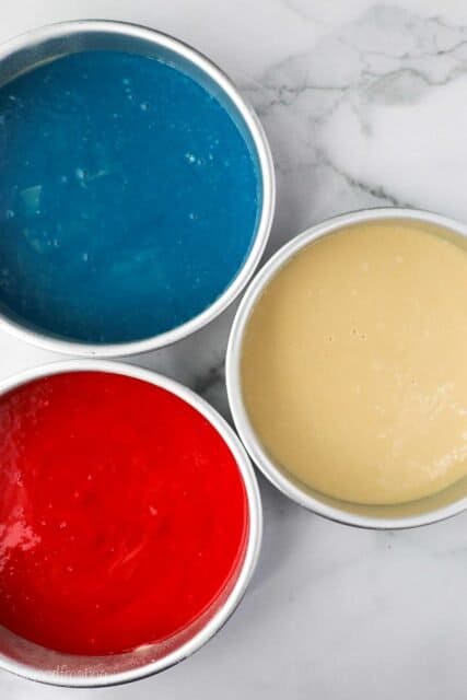 overhead shot of three cake pans filled with batter. One is blue, one is red and one is uncolored