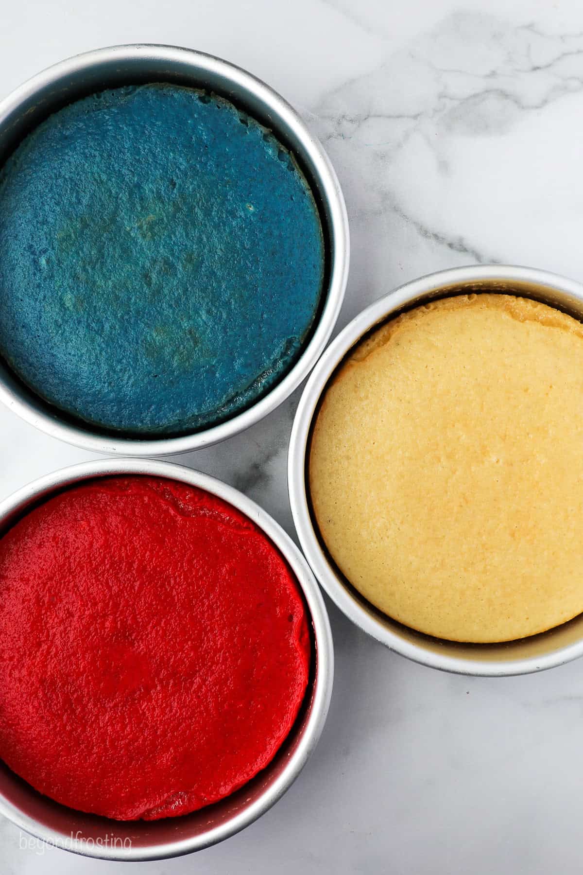 Three baked red, white, and blue cakes in cake pans.