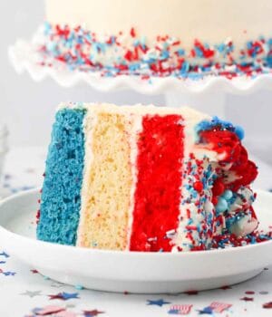 a slice of 3 layer cake with layers of blue, white and red cake. Patriotic confetti on the table.