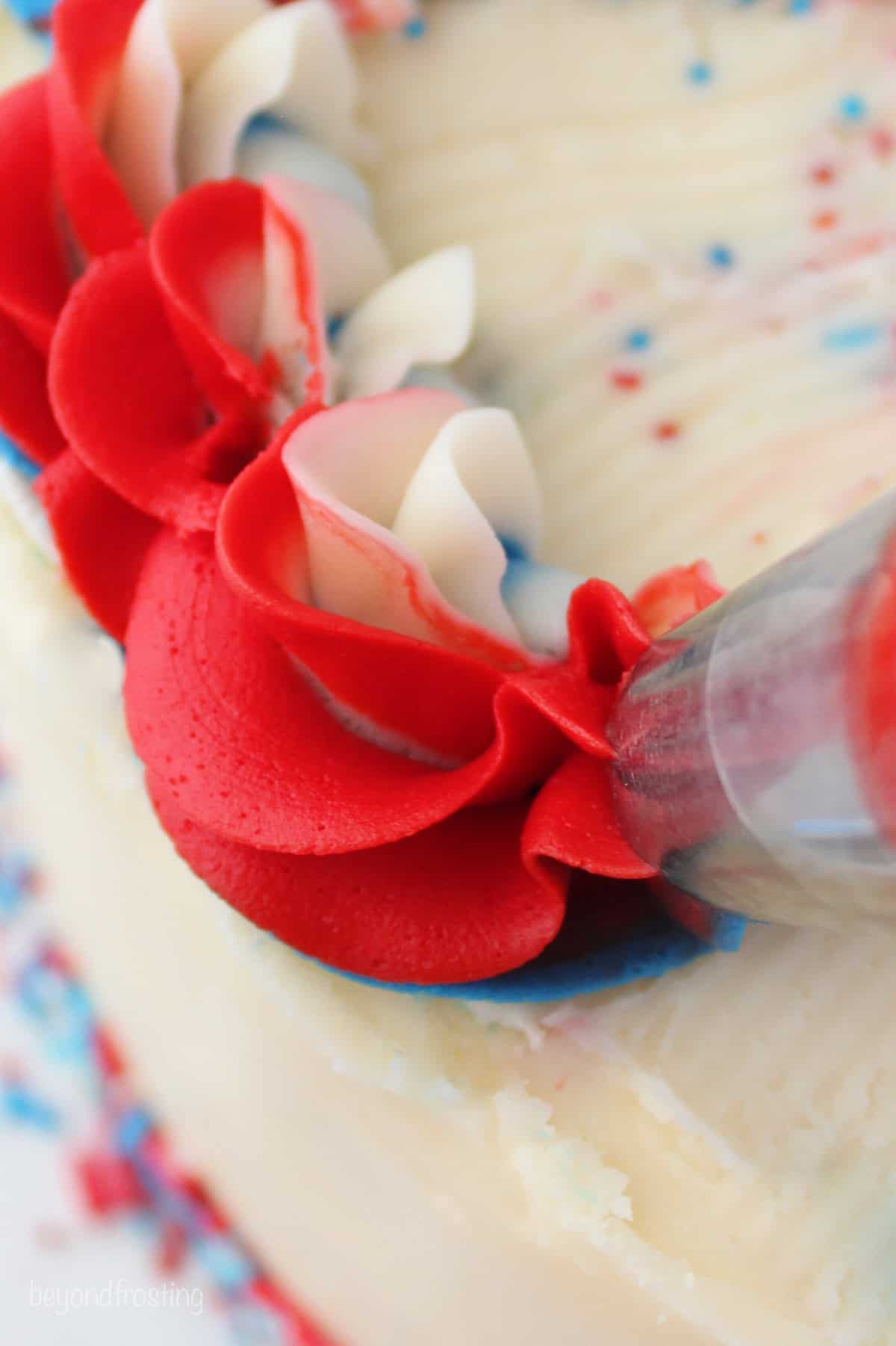 Close up of a piping tip piping a decoration of mutlicolored red, white, and blue frosting onto a cake.