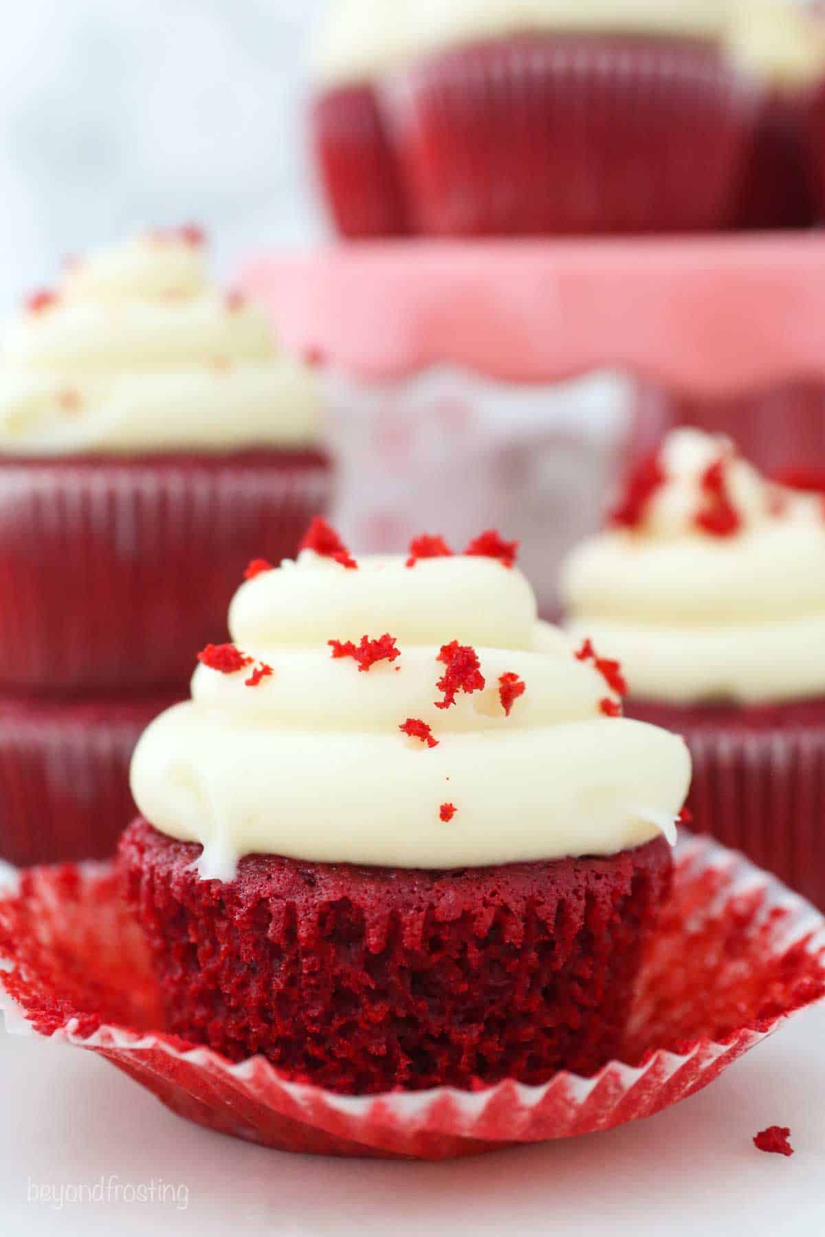 an unwrapped red velvet cupcake frosted with cream cheese frosting, cupcakes in the background too
