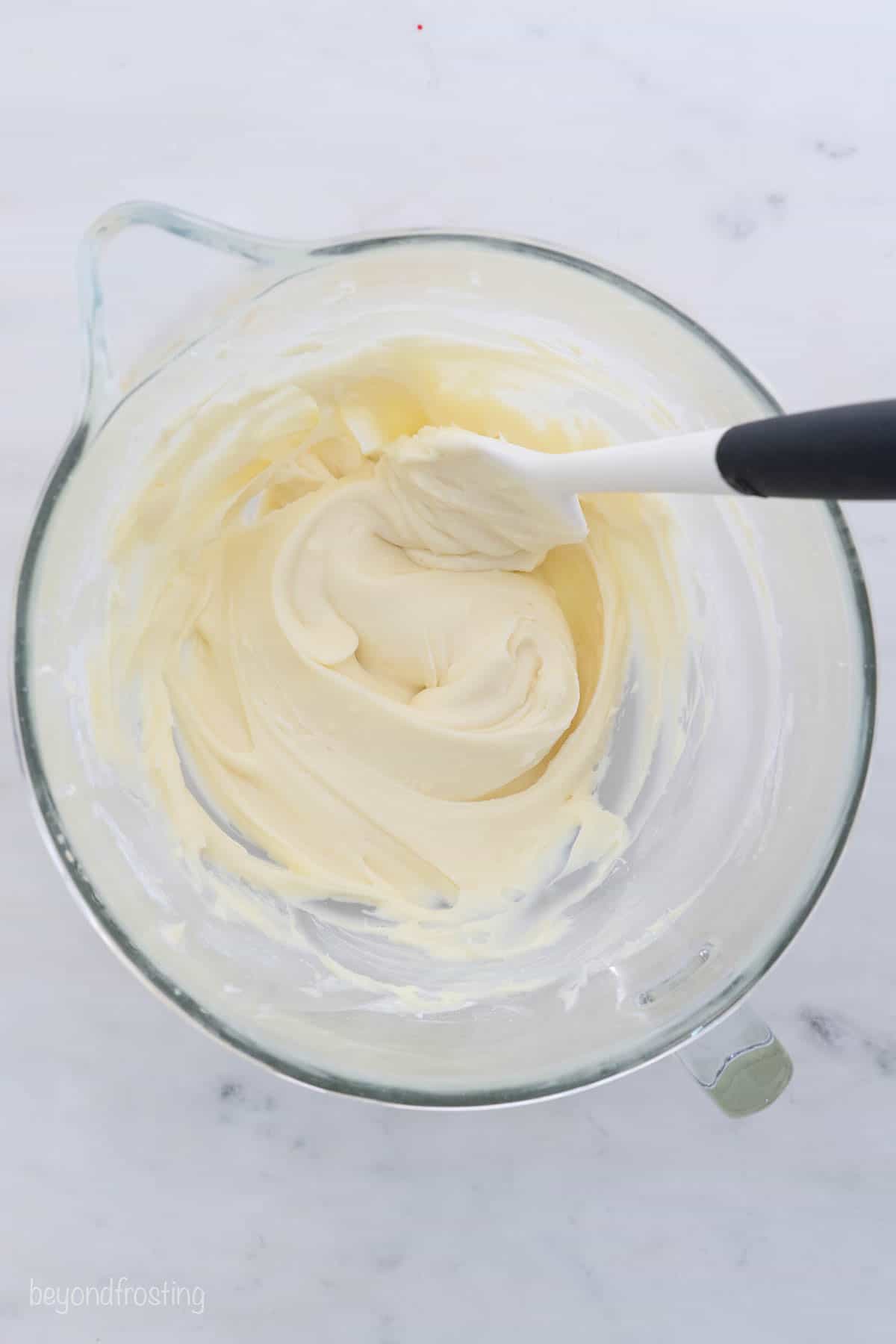overhead view of a glass mixing bowl filled with frosting and a white spatula