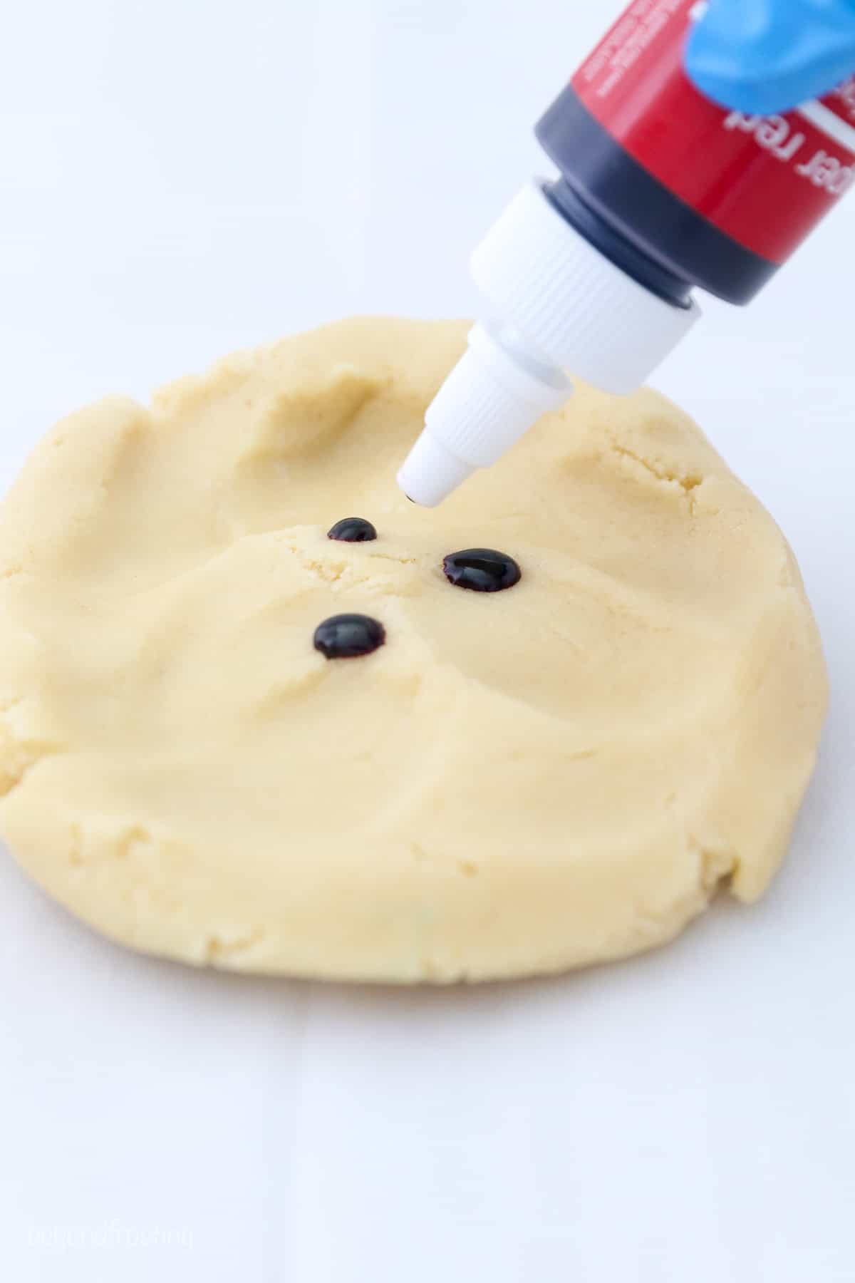 A bottle of blue food coloring adding drops to a piece of cookie dough.