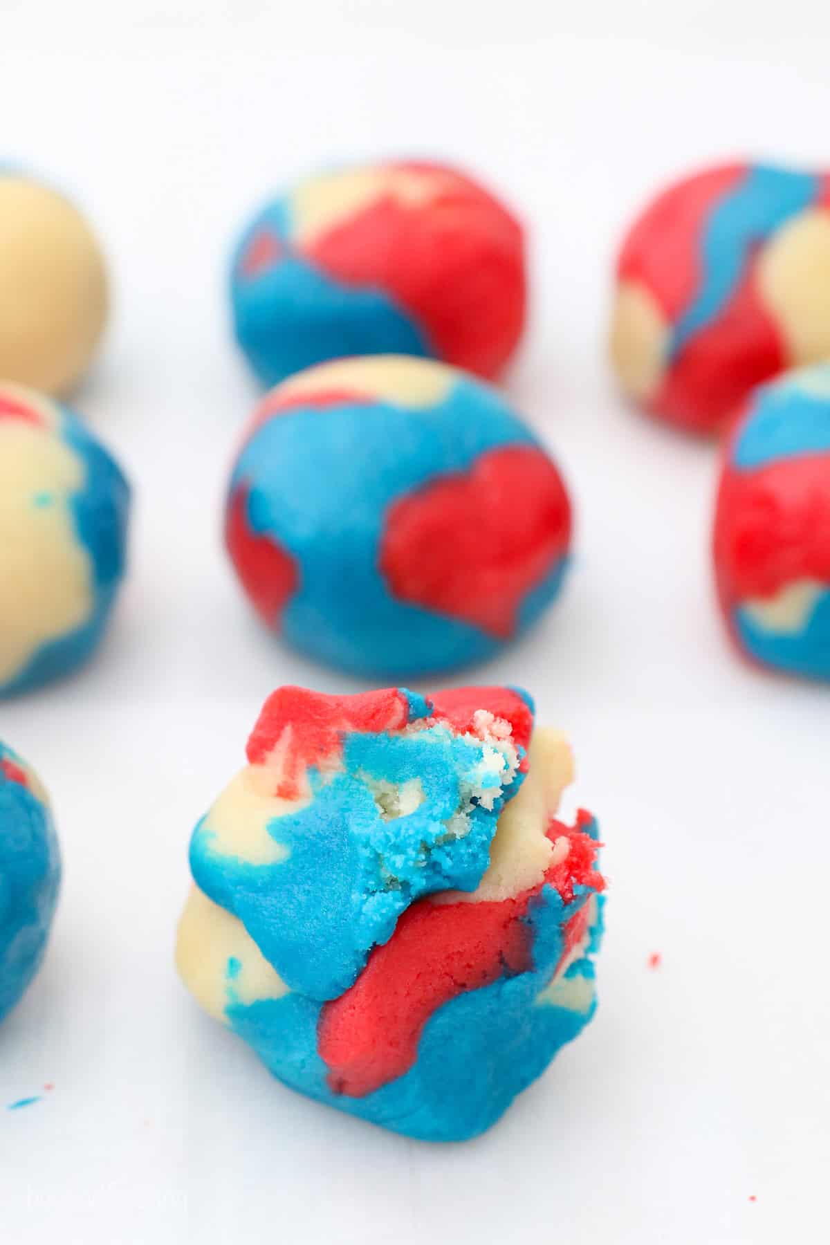 Red, white and blue tye-dyed cookie dough balls arranged in rows.