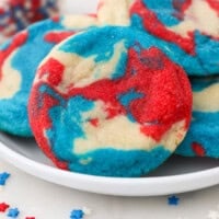 Close up of a tye-dye patriotic sugar cookie propped up against a pile of cookies on a plate.