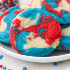 Close up of a tye-dye patriotic sugar cookie propped up against a pile of cookies on a plate.
