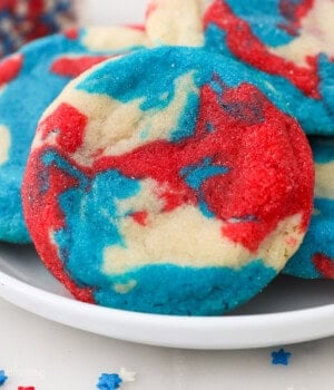 Close up of a tye-dye patriotic sugar cookie propped up against a pile of cookies on a plate.