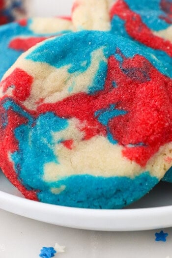 Close up of a tye-dye patriotic sugar cookie propped up against a pile of cookies on a plate.