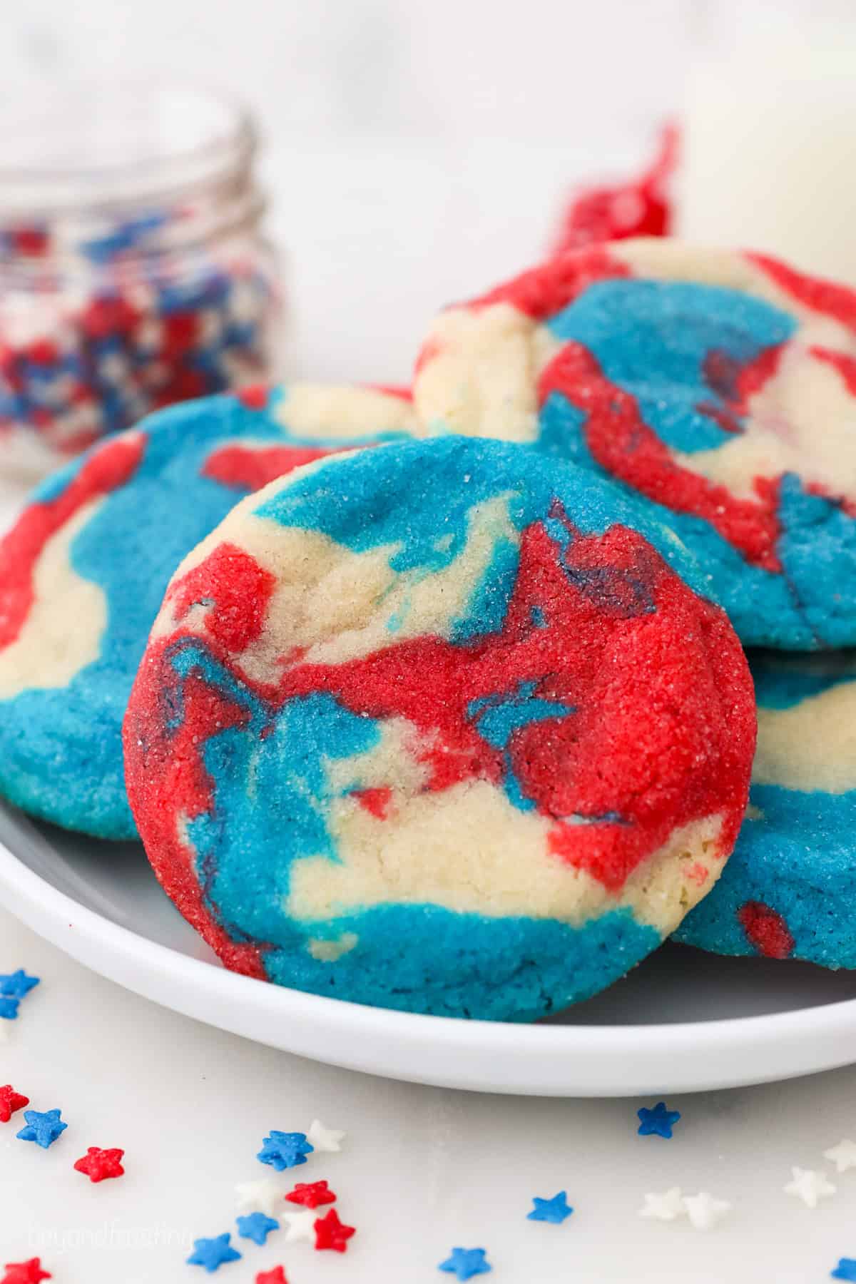 A tye-dye patriotic sugar cookie propped up against a pile of cookies on a plate.
