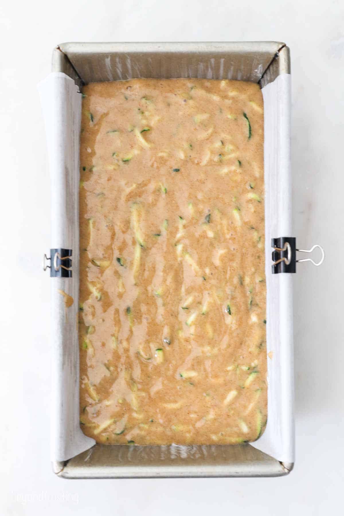 Overhead view of a lined loaf pan filled with homemade zucchini bread batter.