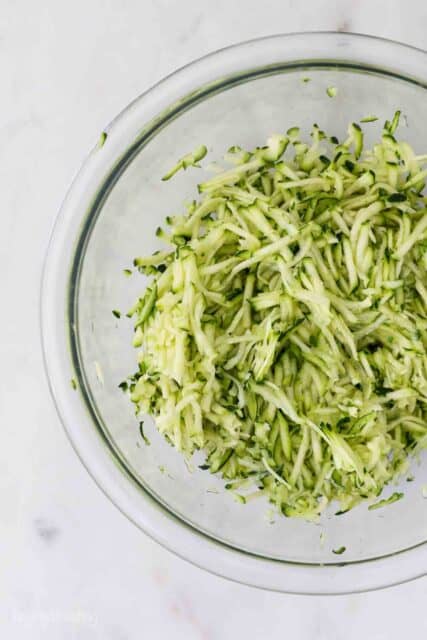 an overhead shot of half a glass mixing bowl filled with shredded zucchini