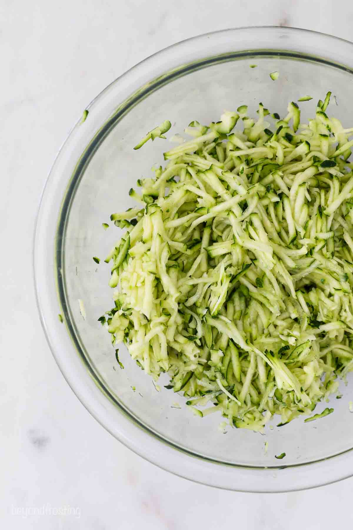 This flavorful zucchini bread recipe makes a soft, moist loaf filled with cozy cinnamon and freshly grated zucchini. Easy to bake and slice! Shredded and drained zucchini in a glass bowl.