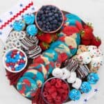 a round wooden board filled with red, white and blue themed desserts like cookies, candies and donuts