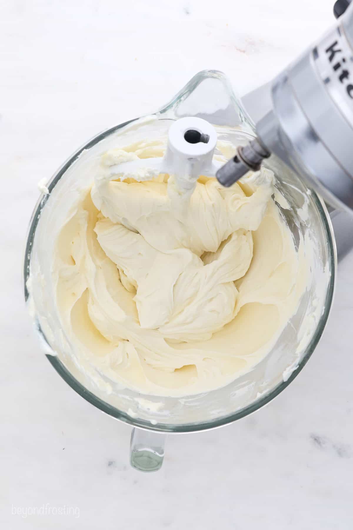 Overhead view of cheesecake batter in the glass bowl of a stand mixer.