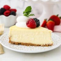 A slice of creamy cheesecake garnished with fresh berries and a swirl of whipped cream on a white plate.