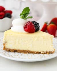 A slice of creamy cheesecake garnished with fresh berries and a swirl of whipped cream on a white plate.