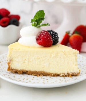 A slice of creamy cheesecake garnished with fresh berries and a swirl of whipped cream on a white plate.