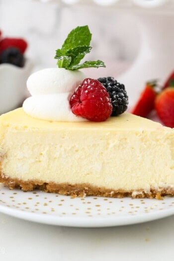A slice of creamy cheesecake garnished with fresh berries and a swirl of whipped cream on a white plate.