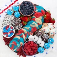 Overhead view of a 4th of July dessert board with red, white, and blue themed candies, cookies, donuts, fruit, and other treats.