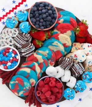 Overhead view of a 4th of July dessert board with red, white, and blue themed candies, cookies, donuts, fruit, and other treats.