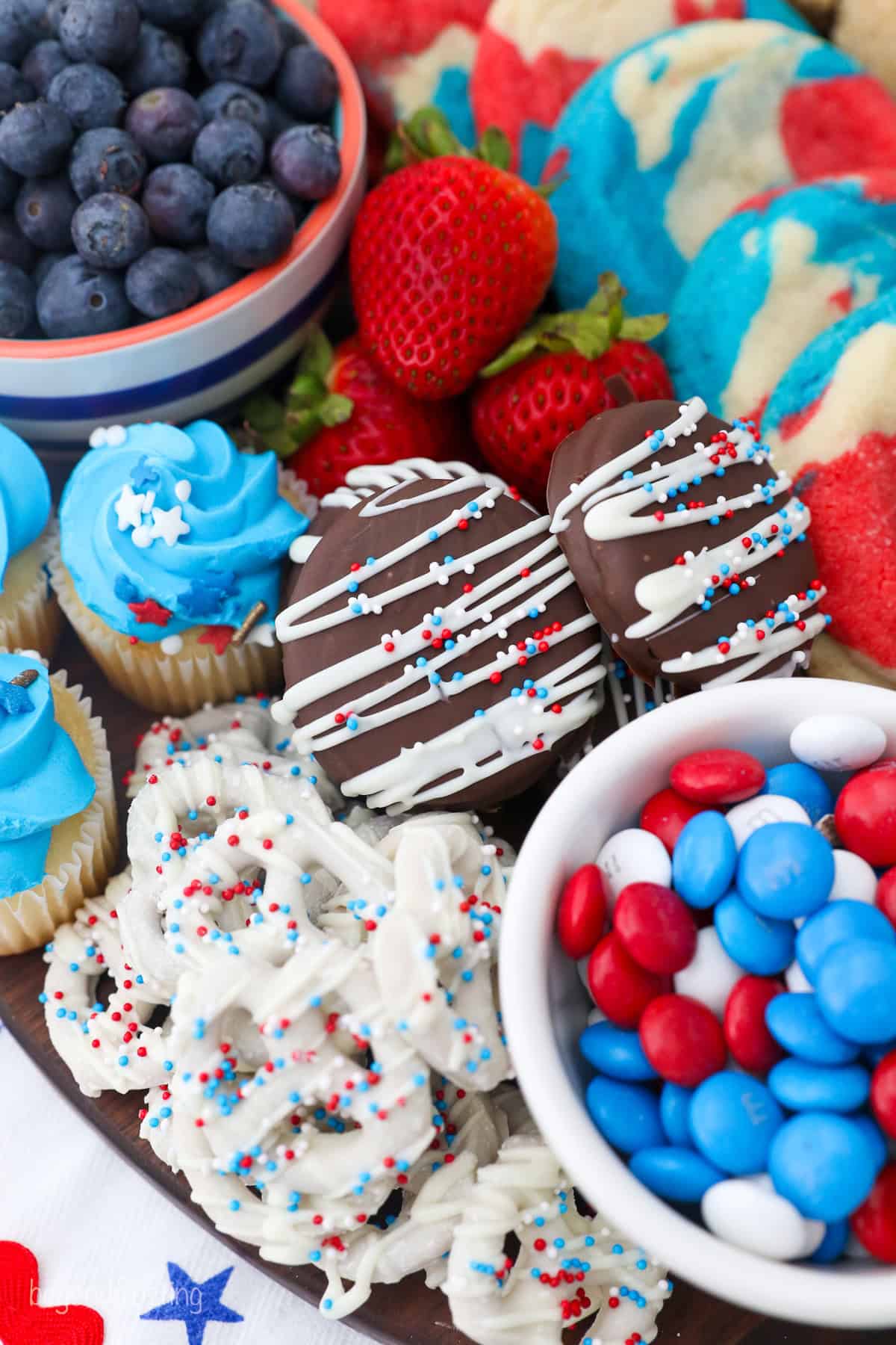 Close up overhead view of a 4th of July dessert board with red, white, and blue themed candies, cookies, donuts, fruit, and other treats.