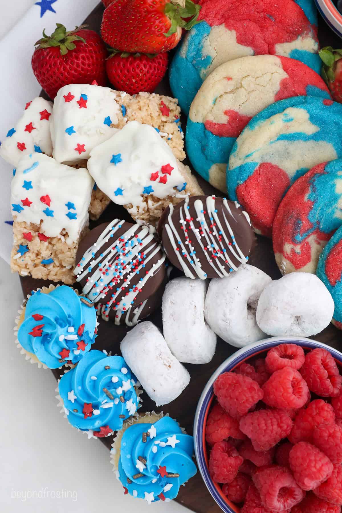 Overhead view of a 4th of July dessert board with red, white, and blue themed cookies, donuts, fruit, and other treats.