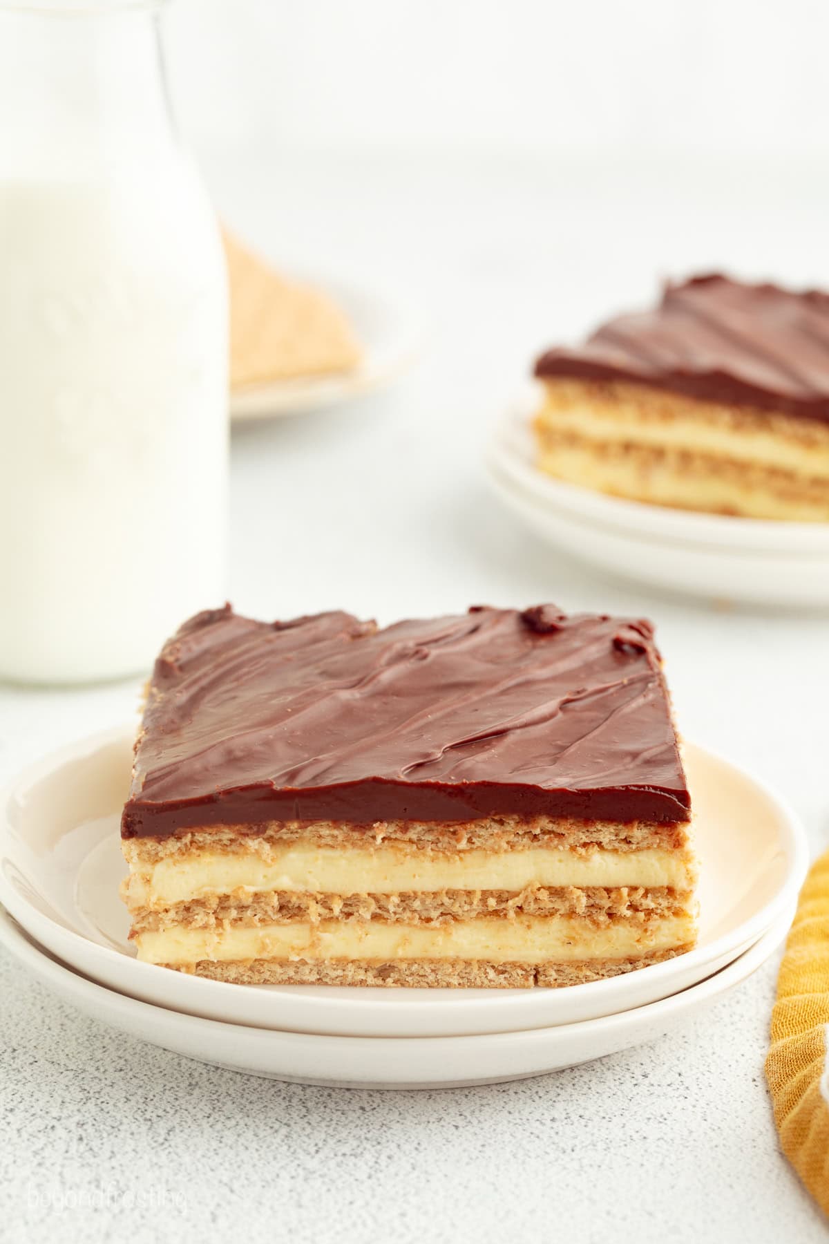 No-bake chocolate eclair cake is an easy icebox cake recipe with a creamy filling stacked with graham crackers, topped with chocolate ganache. A slice of no-bake eclair cake on a plate, showing the creamy layers.