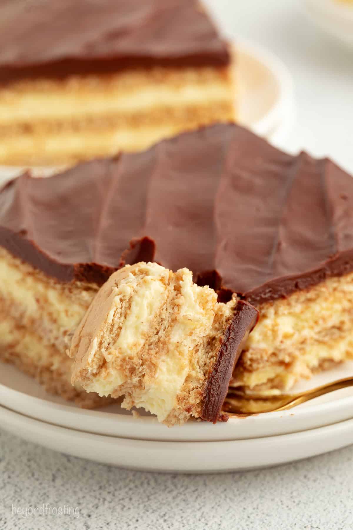 No-bake chocolate eclair cake is an easy icebox cake recipe with a creamy filling stacked with graham crackers, topped with chocolate ganache. A forkful of no-bake chocolate eclair cake next to a slice on a plate.
