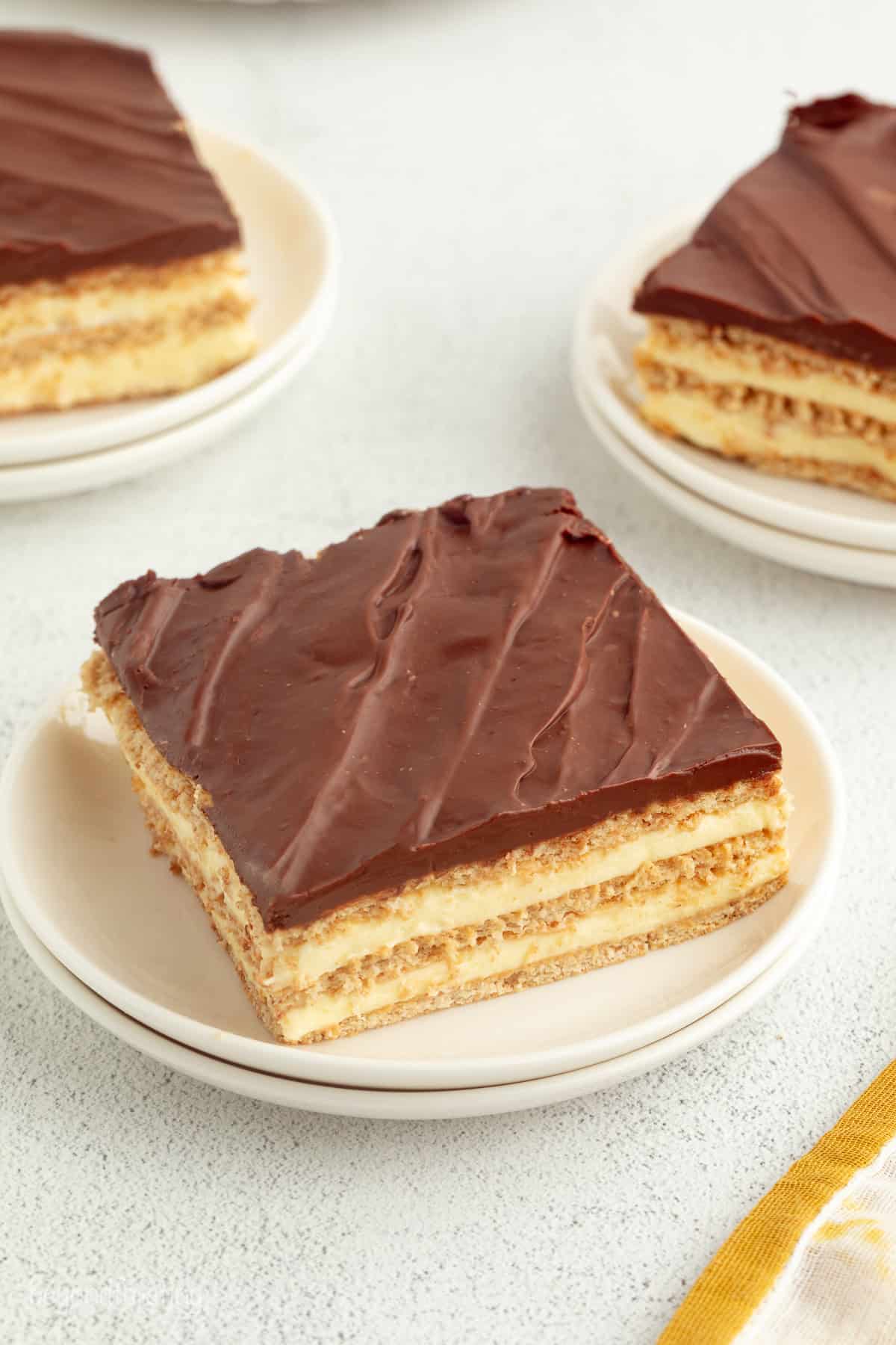 No-bake chocolate eclair cake is an easy icebox cake recipe with a creamy filling stacked with graham crackers, topped with chocolate ganache. A slice of no-bake chocolate eclair cake on a plate.