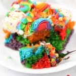 A slice of rainbow cake with one piece on a fork