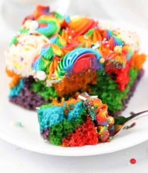 A slice of rainbow cake with one piece on a fork