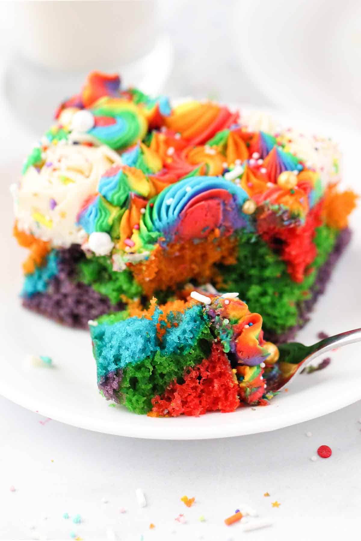 A slice of rainbow cake with one piece on a fork