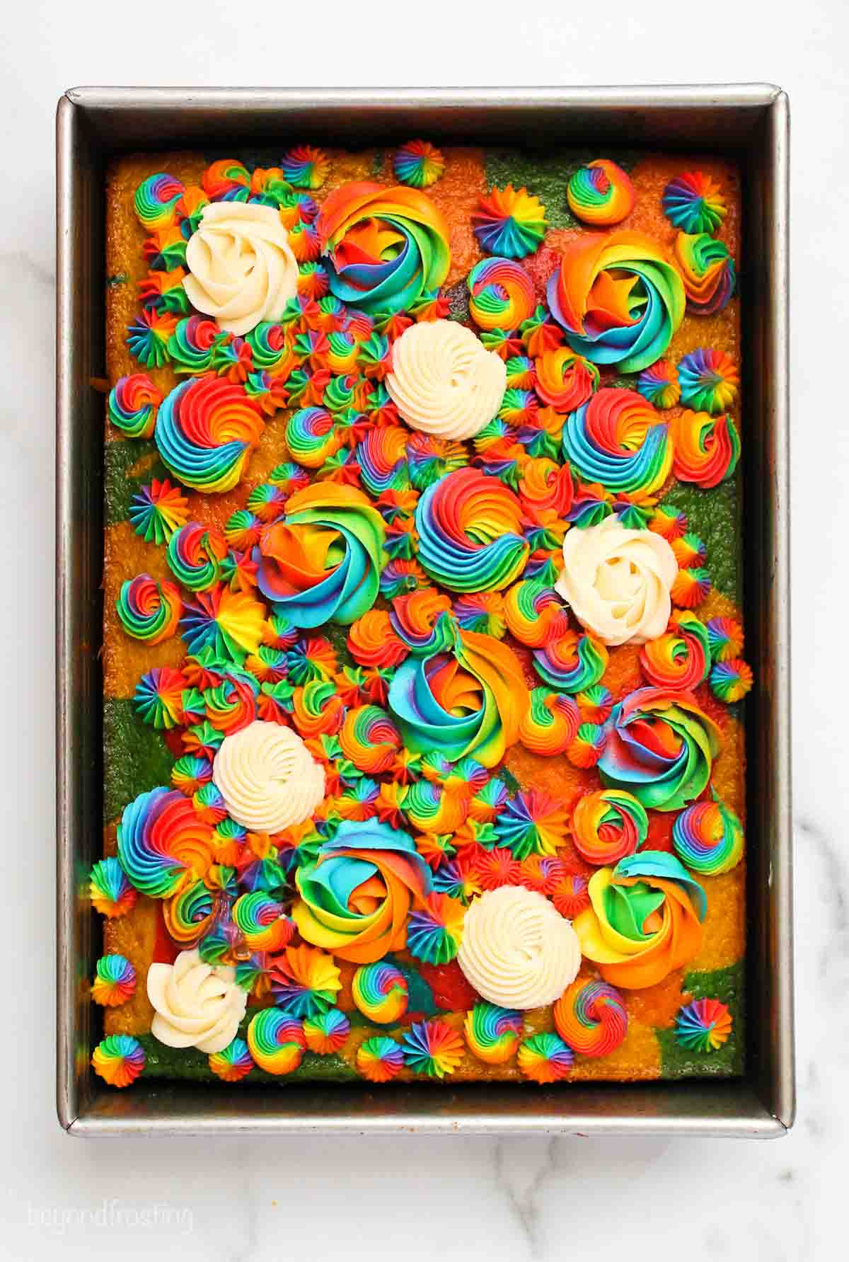 Rainbow cake topped with rainbow and white frosting rosettes