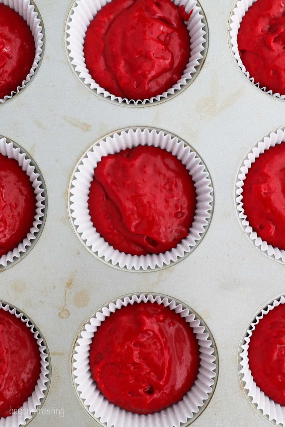 Overhead close up view of a lined cupcake pan filled with red velvet cake batter.