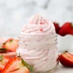 a small mason jar with pipped strawberry frosting surrounded by sliced strawberries