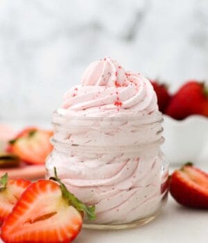 a small mason jar with pipped strawberry frosting surrounded by sliced strawberries