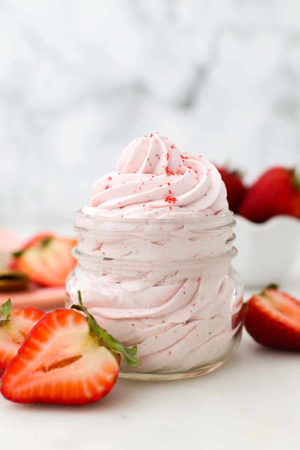 a small mason jar with pipped strawberry frosting surrounded by sliced strawberries