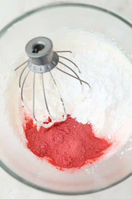 overheat shot of mixing bowl with a wire whisk with whipped cream, powdered strawberries and powdered sugar